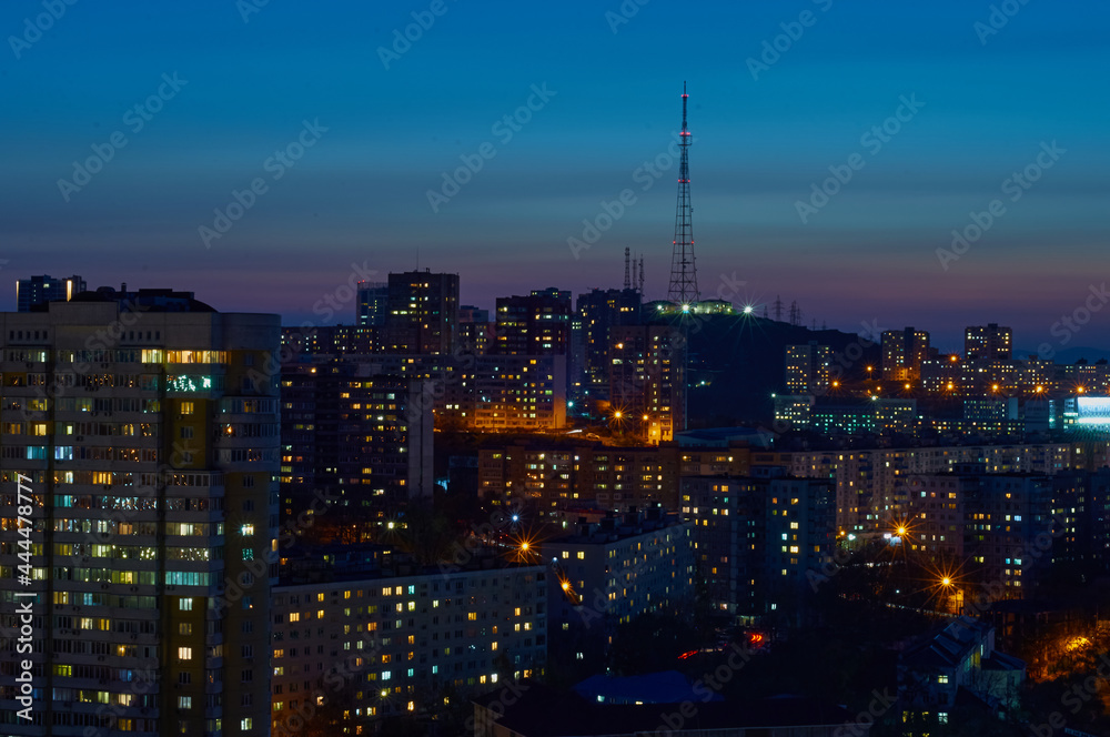 Aerial view of the night city of Vladivostok, Russia. TV tower on a hill, sea bay and mountain range.