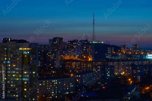 Aerial view of the night city of Vladivostok, Russia. TV tower on a hill, sea bay and mountain range.