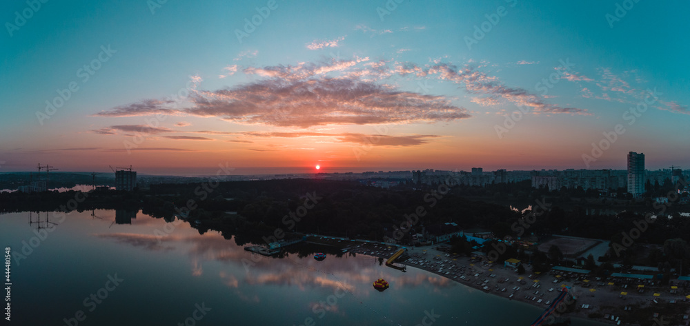 Scenic aerial sunrise panorama with clouds reflecting in mirror water surface on wide river. Early morning, dawn in Kharkiv Zhuravlivskyy Hidropark from sky. Drone color graded photography