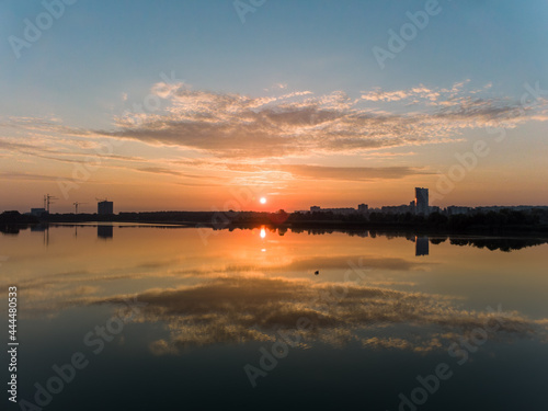 Scenic aerial sunrise with clouds reflecting in mirror water surface on wide river. Early morning, dawn in Kharkiv Zhuravlivskyy Hidropark from sky. Drone photography