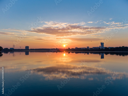 Scenic aerial sunrise with clouds on blue sky reflecting in mirror water surface on wide river. Early morning, dawn in Kharkiv Zhuravlivskyy Hidropark from sky. Drone photography