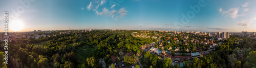 Aerial evening wide panoramic view on green summer Kharkiv city recreation park Sarzhyn Yar. Botanical garden playground and church in residential Shatilovka district area in sunset light © Kathrine Andi