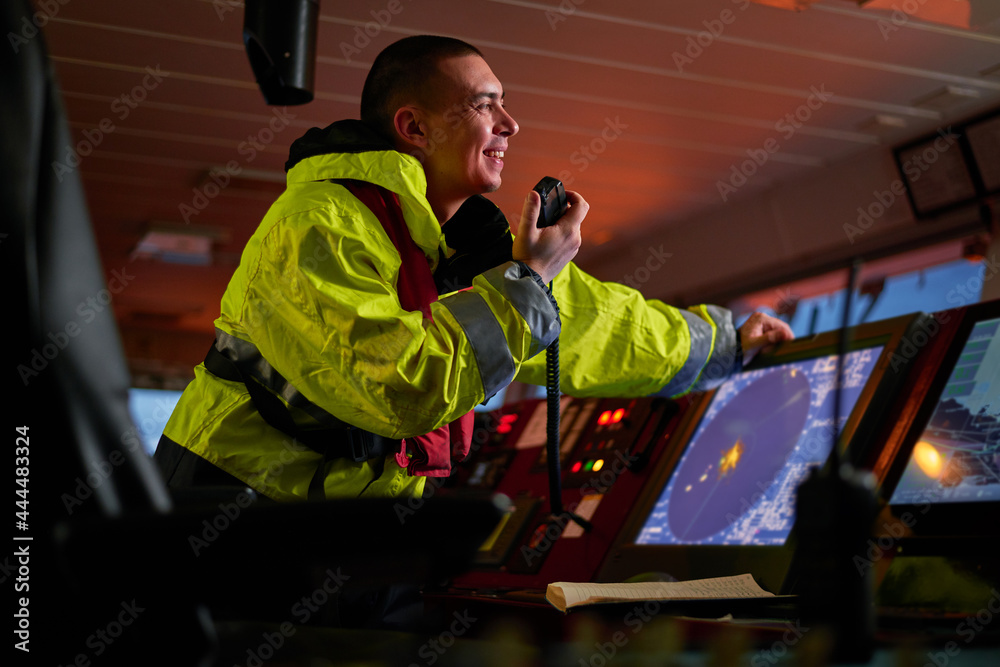 Navigator. pilot, captain as pat of ship crew performing daily duties with VHF radio, binoculars on board of modern ship with high quality navigation equipment on the bridge on sunrise. Navigator. pilot, captain as pat of ship crew performing daily duties with VHF radio, binoculars on board of modern ship with high quality navigation equipment on the bridge on sunrise.