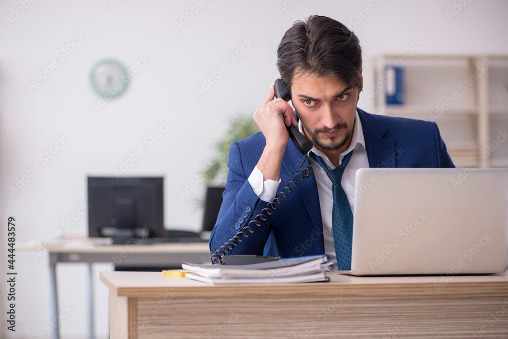 Young male employee unhappy with excessive work in the office Young male employee unhappy with excessive work in the office
