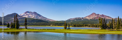 Panoramic view of mountain lake surrounded by fir trees and volcanic mountain peaks.