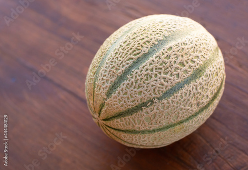 A ripe cantaloupe melon with a textured surface and dark stripes is on a wooden table.