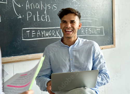 Young happy indian latin man student with laptop laughing during college seminar class. Smiling llatin Hispanic businessman enjoying creative brainstorm in modern contemporary office at meeting. photo