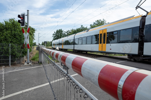 Selective focus view at red and white level crossing railway barrier which block the road and regional train move on the rail on countryside in Germany.	