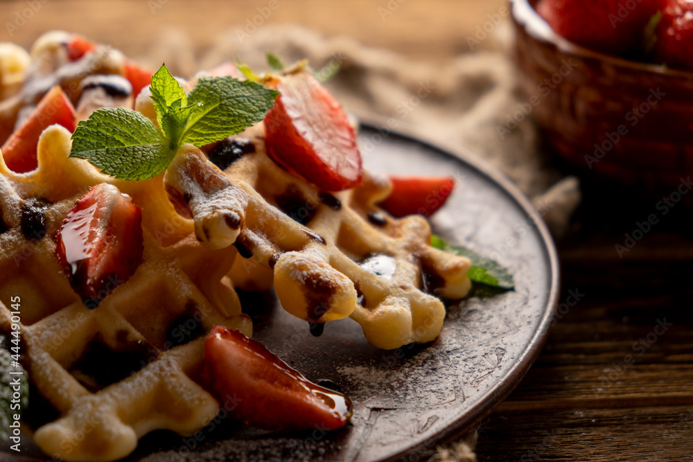 Waffles with strawberries, chocolate topping and powdered sugar on wooden table