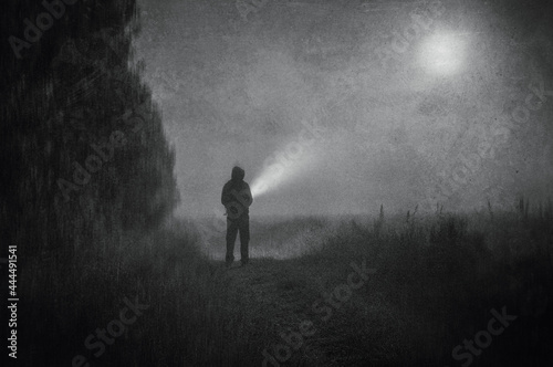 A moody atmospheric concept, of a spooky figure standing in a field with a torch on a foggy spooky night. With a grunge, vintage black and white edit © Dave