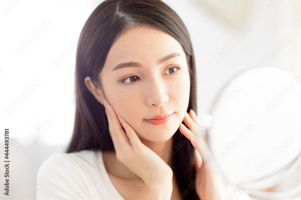 Young woman touching face skin and looking in mirror Young woman touching face skin and looking in mirror