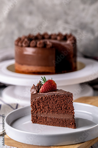 Slice of delicious homemade chocolate cake soft fudge topping with strawberry on white plate.