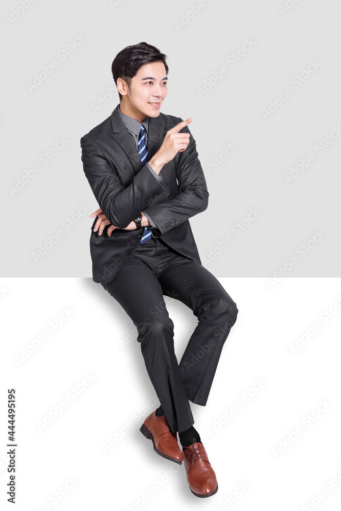 Young business man sitting on blank panel and showing something Young business man sitting on blank panel and showing something