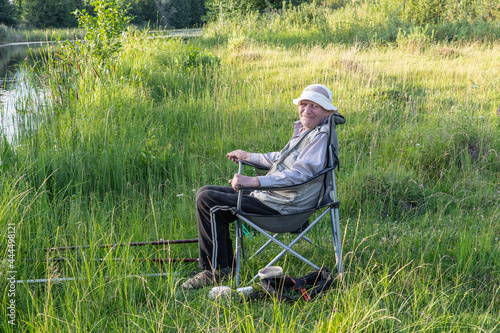 An elderly fisherman on the bank of a quiet river enjoys fishing. © Oleg