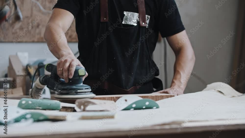 Man worker grinding a wooden plank in the workshop using an instrument Man worker grinding a wooden plank in the workshop using an instrument