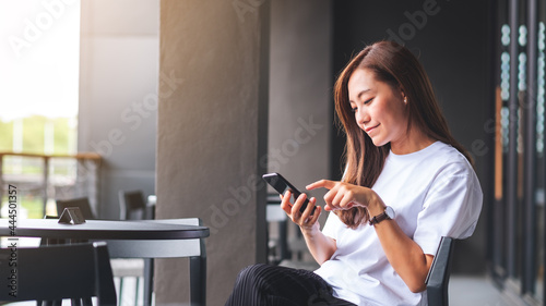Fotografie A beautiful young asian woman holding and using mobile phone