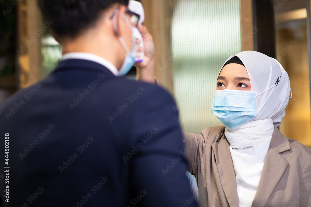 Receptionist asian muslim woman use thermometer gun to measure body temperature. Infrared thermometer equipment to check temperature on the forehead. epidemic virus outbreak.
