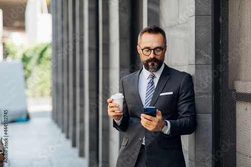 Portrait Stylish hipster bearded business man in suit drinking coffee and use smartphone. Peoples addicted to technology