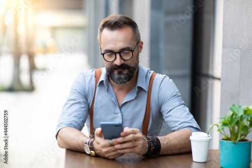 Portrait Stylish hipster bearded man drinking coffee and use smartphone. Peoples addicted to technology