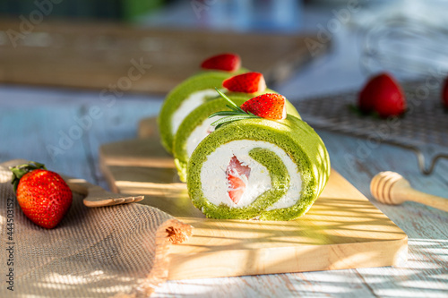 Fotografi Matcha green tea roll cake with fresh cream topping with strawberry paste on wooden board