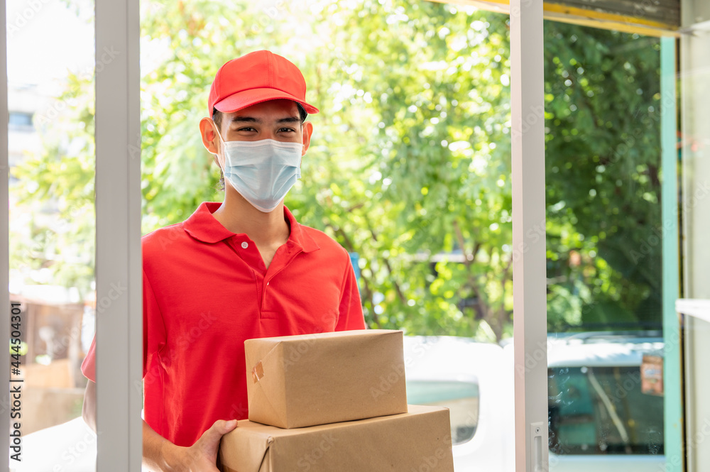 Portrait of Asian delivery man in uniform wearing face mask and holding small box package, smiling and looking at camera. Product logistic service and delivery during coronavirus pandemic concept. Portrait of Asian delivery man in uniform wearing face mask and holding small box package, smiling and looking at camera. Product logistic service and delivery during coronavirus pandemic concept.