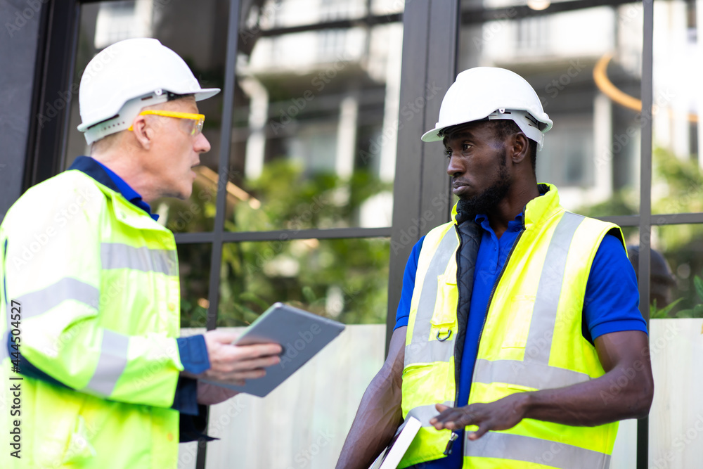 Two engineers African american engineer and caucasian electrician wearing white hard hat walk in new building holding solar panel on hand and Discuss Work Two engineers African american engineer and caucasian electrician wearing white hard hat walk in new building holding solar panel on hand and Discuss Work