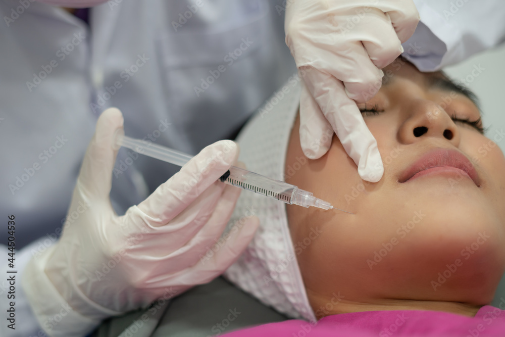 Naklejka premium close-up photo of hands in glove get injection to asian female face,botox,ciliclon,filler injection