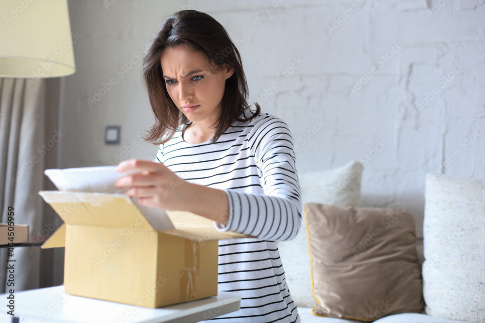 Beautiful young woman is holding cardboard box and unpacking it sitting on sofa at home. Beautiful young woman is holding cardboard box and unpacking it sitting on sofa at home.