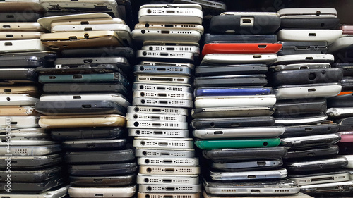 Background of damaged mobile phones. A bunch of broken smartphones. Used phones stacked on top of each other. Repair services and maintenance of equipment.