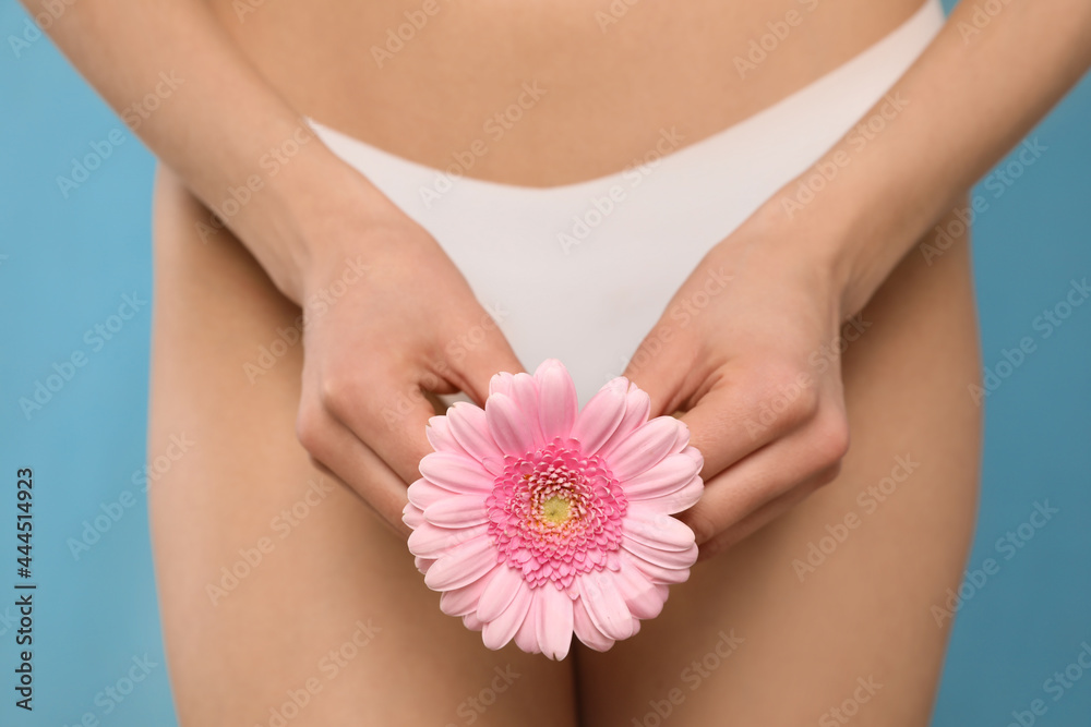 Woman in white panties with gerbera flower on light blue background, closeup