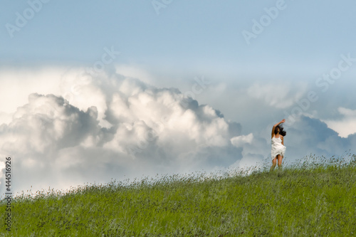 asian long haired woman in white dress on the meadow frozen in motion with a raised hand against сumulus clouds