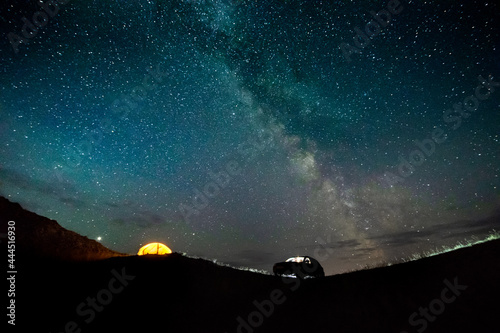 the traveling car and the orange tent with light inside on the horizon under the starry night sky