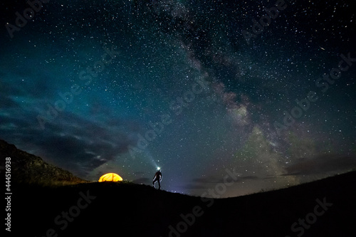 orange tent with light inside with a silhouette of a man with headlamp on the background of a universe
