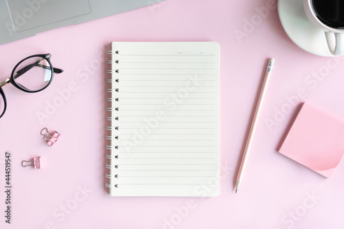 Flat lay of a cup of coffee, glasses, laptop and office stationary of businesswoman on pink desk in office. Business and technology concept top view and copy space.
