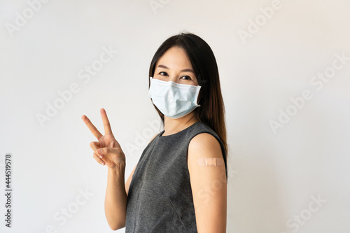 Portrait of beautiful woman wearing surgical mask smiling with happy face at the camera doing victory sign. Asian female pointing two fingers after getting second dose of Covid-19 vaccine. Copy space.