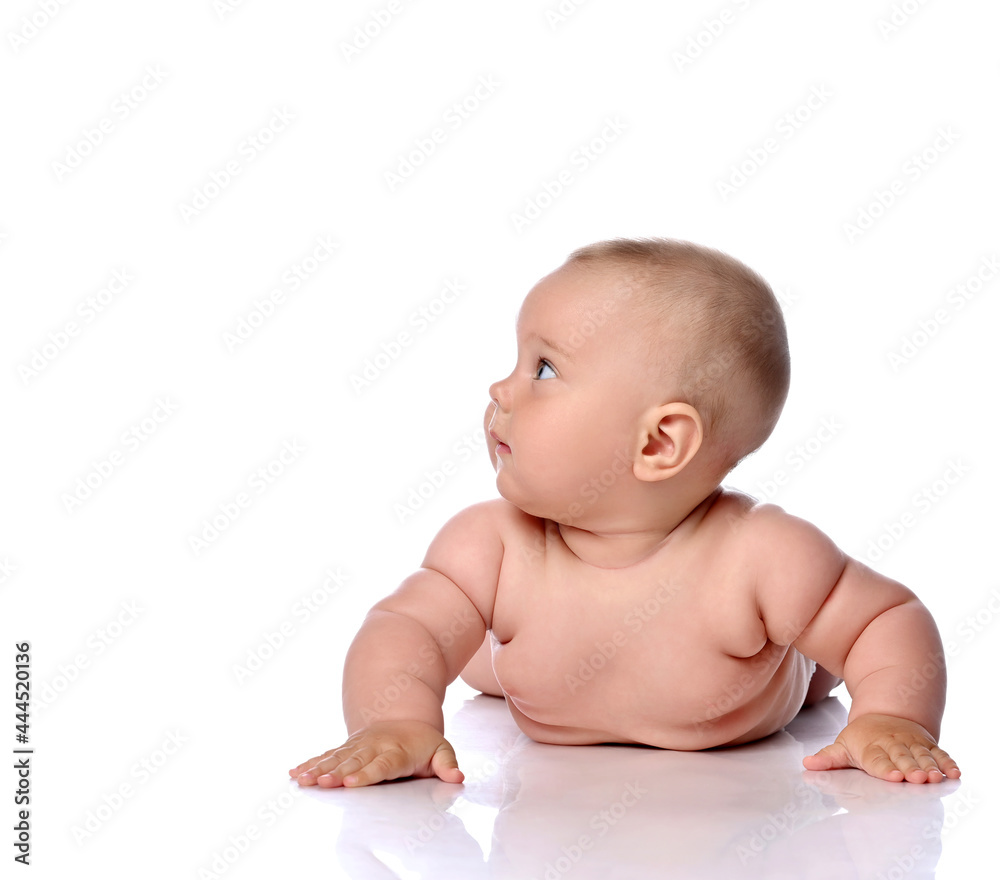 Curious infant child baby girl kid in diaper is lying on her tummy, stomach leaning, rising on hands and looking at upper corner at copy space isolated on a white background Curious infant child baby girl kid in diaper is lying on her tummy, stomach leaning, rising on hands and looking at upper corner at copy space isolated on a white background
