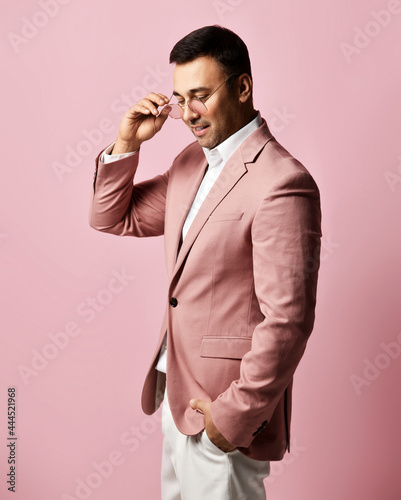 Canvas Print Portrait of young smiling brunet businessman, charismatic art dealer in official suit stands taking off, putting on his golden glasses and talking