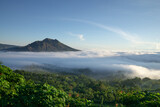 The atmosphere of Mount Batur in the morning where the caldera is covered by low stratus clouds. The sky looks bright blue and green vegetation around Mount Batur