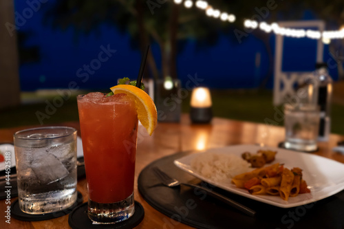 A glass of cocktail and dinner food from the beach bar in hotel with a beautiful night view in the background