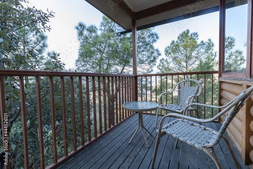 A scenic view of a balcony having wooden railing and easy chairs and an open and green view all around 