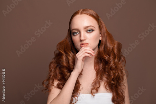 Attractive redhead model with healthy skin and long red hair on brown background
