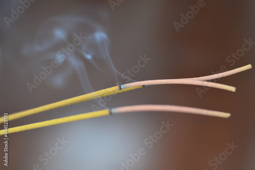 Three lighted incense sticks emitting smoke on a blurred brown background