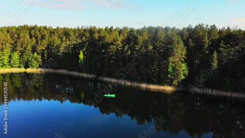 Aerial circle around Fisherman with fishing rod fishing in green boat in scenic Lithuanian countryside lake photo