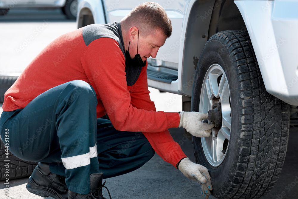 A man changes a wheel on a car on the street on a sunny day. Help on the road with a tire puncture. A man changes a wheel on a car on the street on a sunny day. Help on the road with a tire puncture.