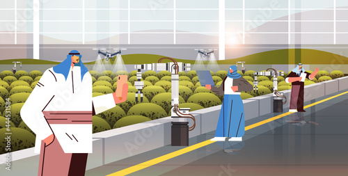 arab farmers controlling agricultural drones sprayers quad copters flying to spray chemical fertilizers in greenhouse
