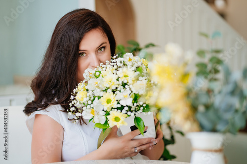 attractive woman in white clothes with flowers at the table in a light room. 