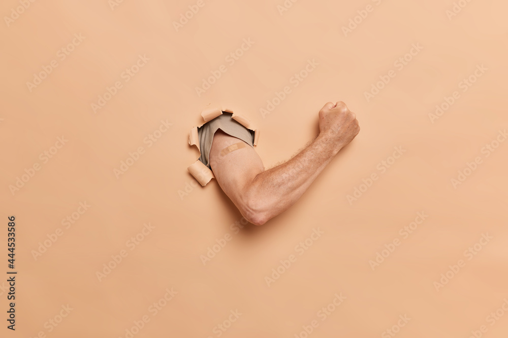 The muscled hairy hand of a man in polo breaks through the wall with