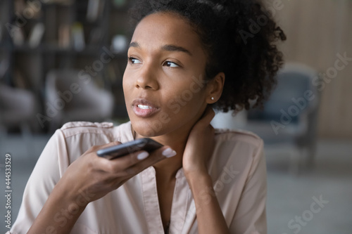 Close up smiling African American woman recording audio message on smartphone, holding phone near mouth, confident businesswoman chatting online by speakerphone, activating digital assistant