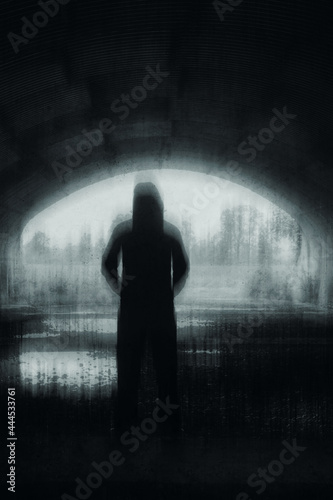 A strange hooded figure  silhouetted at the entrance to a tunnel. With a spooky  black and white vertical edit