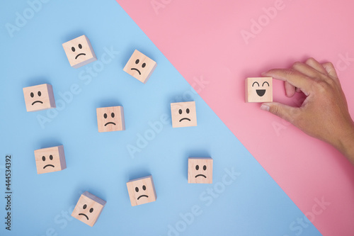 Hand holding wood cube with smiley face icon symbol on blue and pink background. Customer service rating, Satisfaction survey concept.
